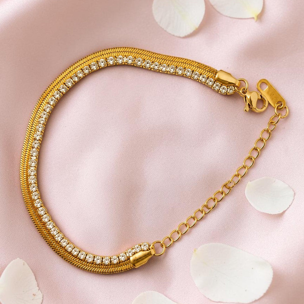 Gold tone bracelet with crystals on a pink surface with white petals