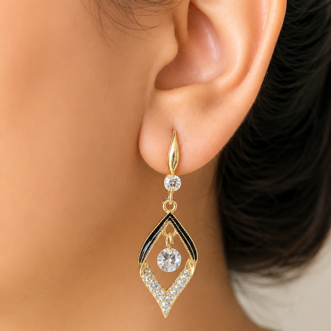 A gold drop earring with a clear central gemstone and black enamel accents, shown worn on a person's ear.