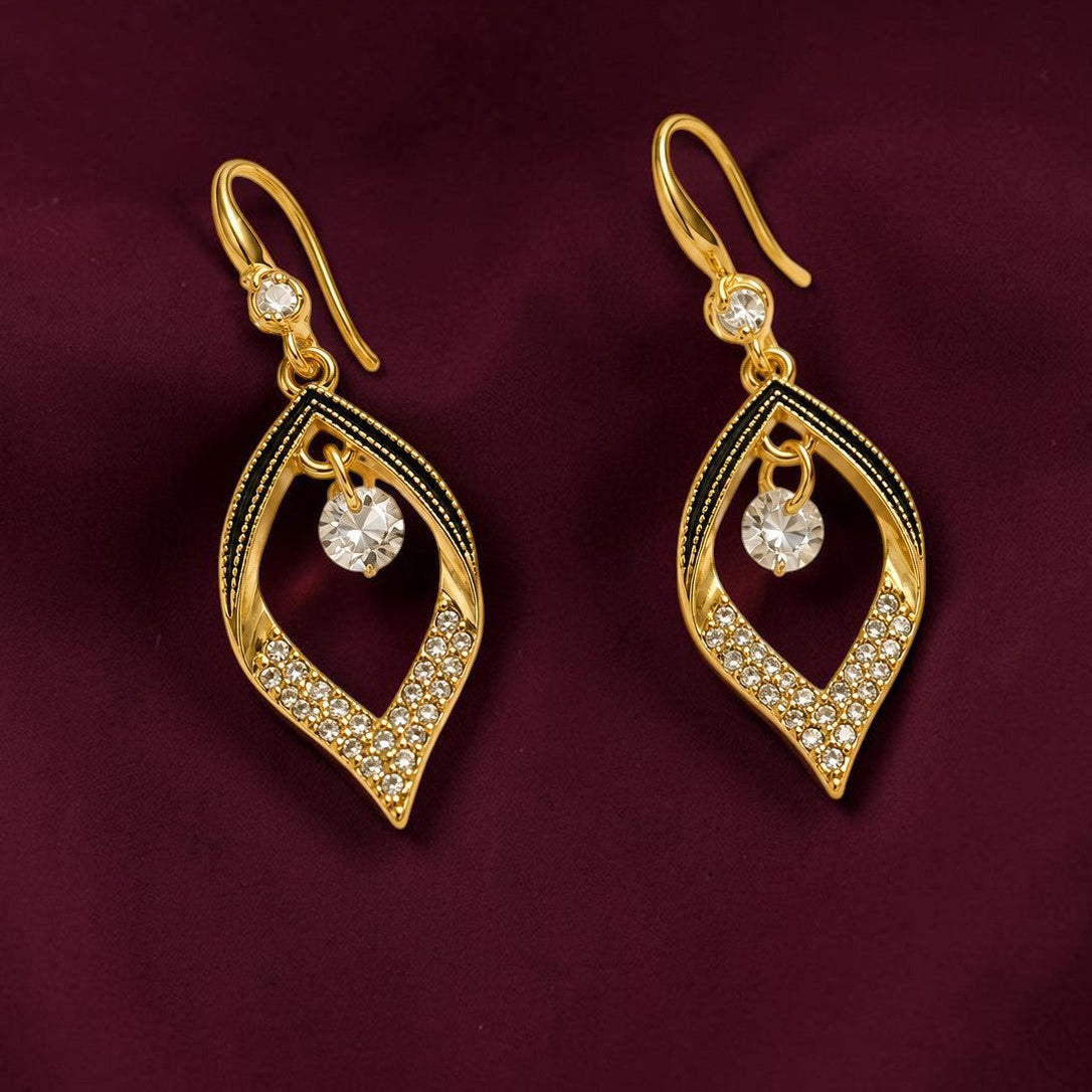 A pair of gold drop earrings with a leaf-like teardrop design, adorned with clear pavé stones and a central clear round gemstone, displayed on a dark burgundy fabric background.