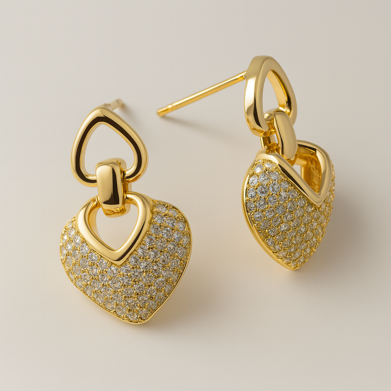 Gold tone heart-shaped earrings with diamond-like stones on a beige background