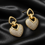 Gold tone heart-shaped earrings with diamond accents on a black satin background