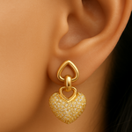 Gold tone heart-shaped earring worn on an ear with a blurred background