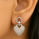 Silver heart-shaped earring worn on an ear with a blurred background