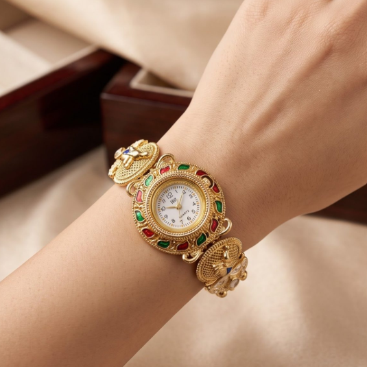 A close-up of a person's wrist wearing an ornate gold watch with colorful enamel details and a white dial, set against a soft beige fabric background.
