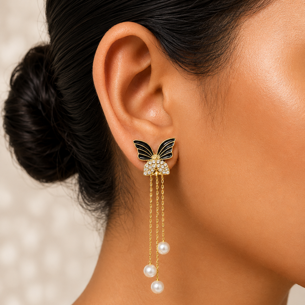 Close-up of a woman wearing a butterfly earring with pearl drops against a neutral background.
