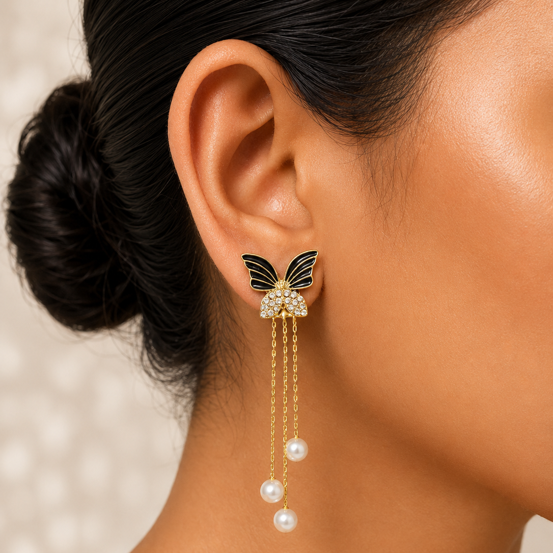 Close-up of a woman wearing a butterfly earring with pearl drops against a neutral background.