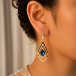 Close-up of a person wearing a diamond earring with a blue gemstone.