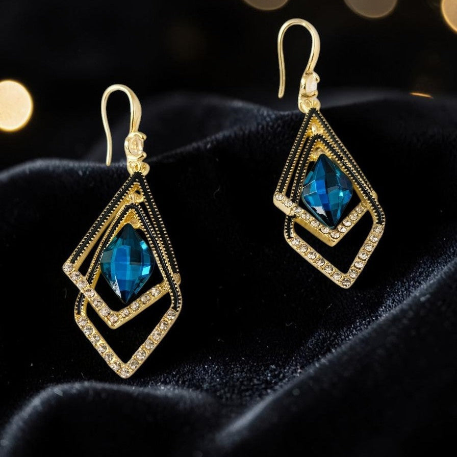 Golden earrings with blue gemstones on a black velvet background