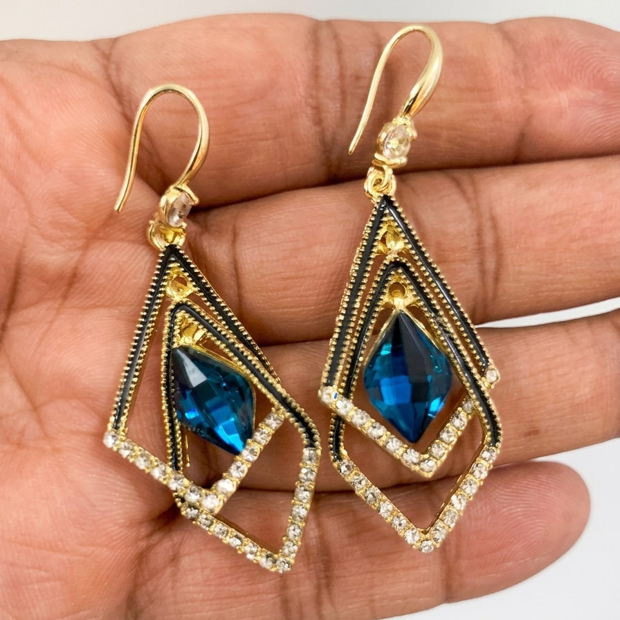 Gold and blue gemstone earrings held in a hand against a white background