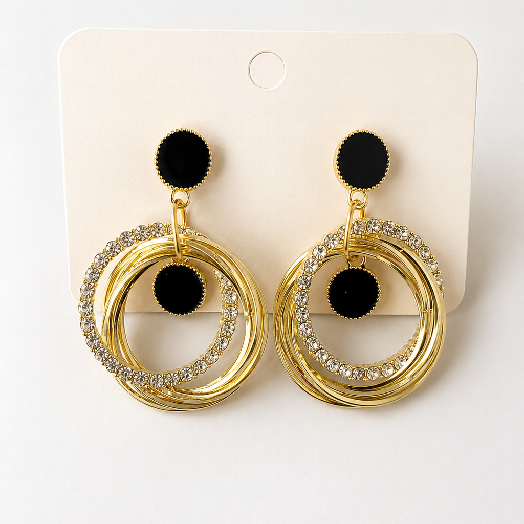 Golden hoop earrings with black pom-poms on a white card