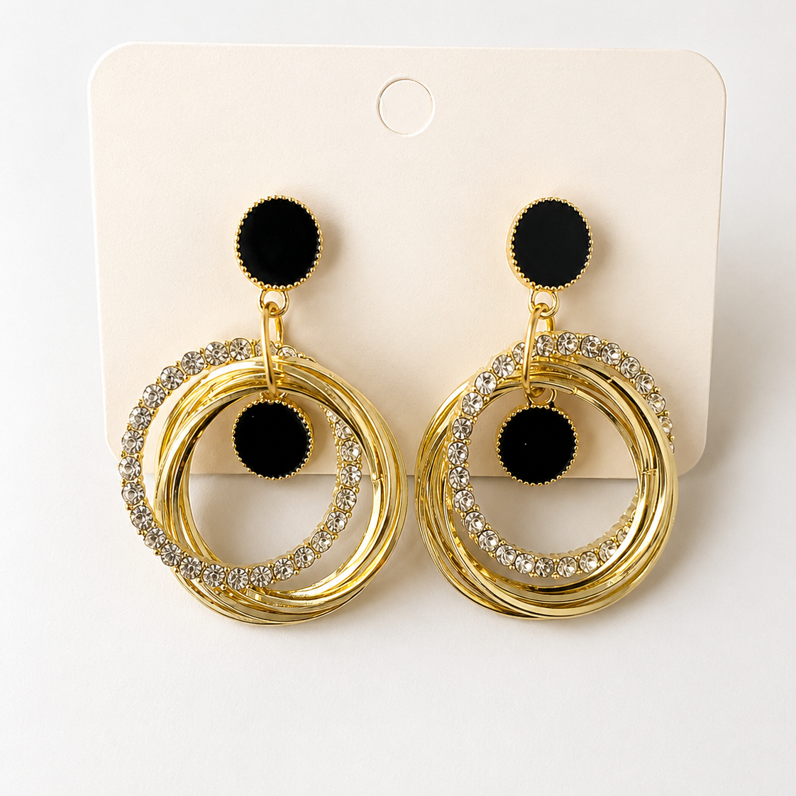 Golden hoop earrings with black pom-poms on a white card