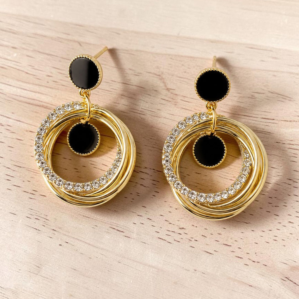 Golden hoop earrings with black centers on a light wooden surface