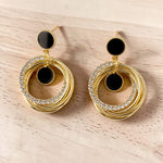 Golden hoop earrings with black centers on a light wooden surface