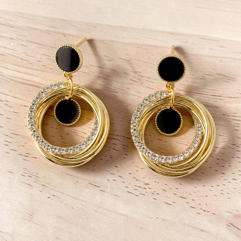 Golden hoop earrings with black centers on a light wooden surface