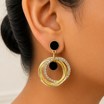 Gold and black circular earring worn by a person with a neutral background