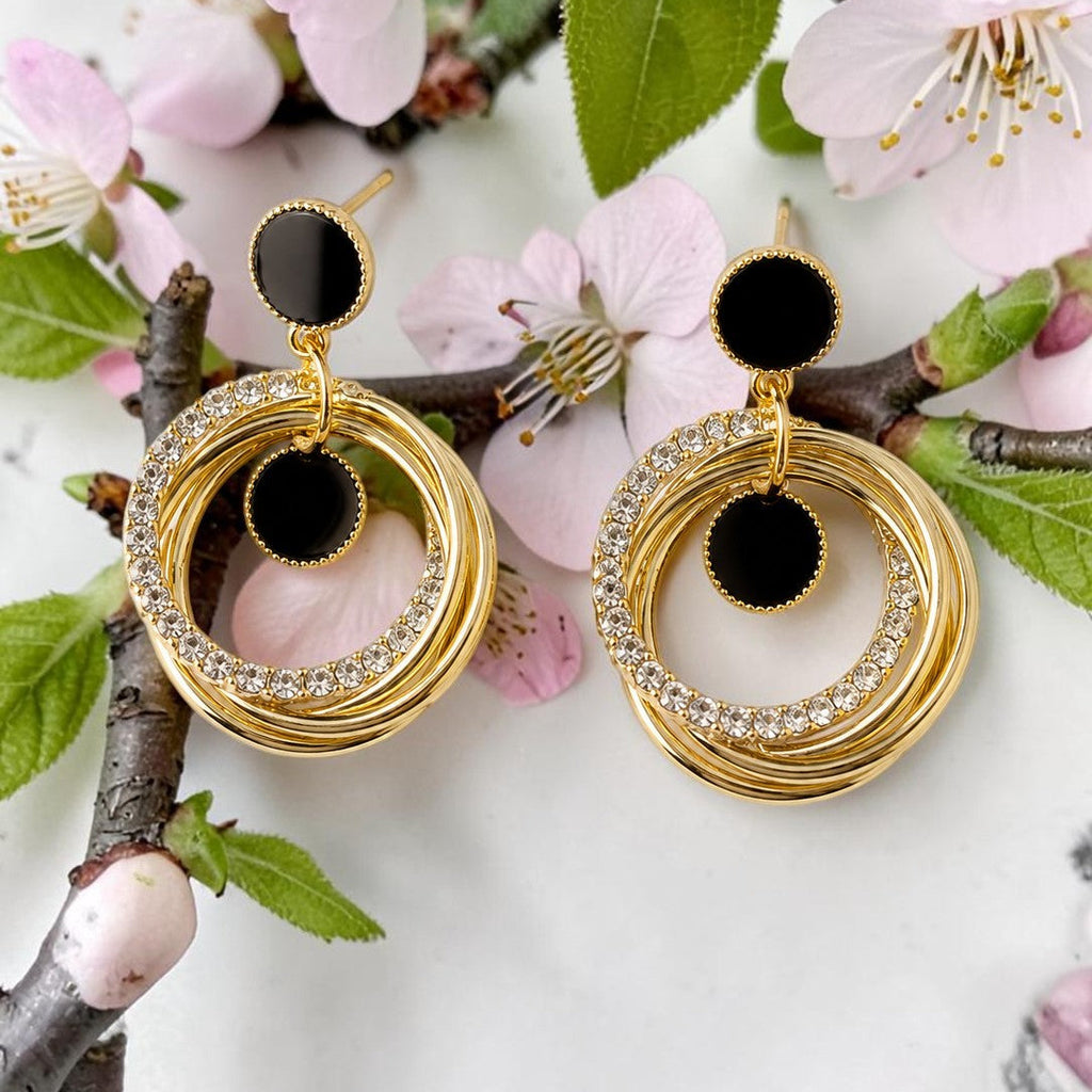 Golden hoop earrings with black centers on a branch with pink flowers