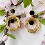 Golden hoop earrings with black centers on a branch with pink flowers