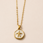 Gold tone necklace with a starfish pendant on a beige background