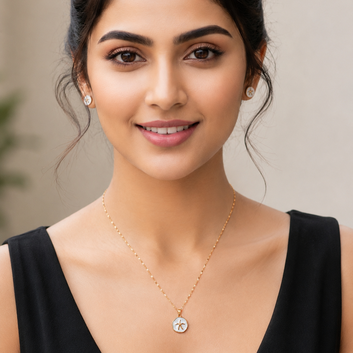 Woman wearing a gold tone necklace with a pendant against a neutral background