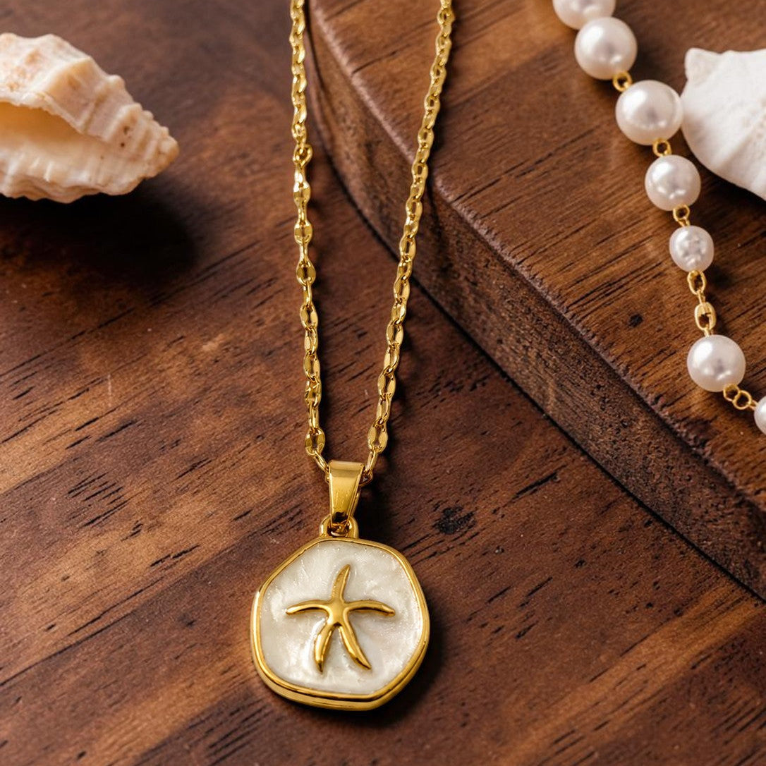 Gold tone necklace with a starfish pendant on a wooden surface with pearls and shells.
