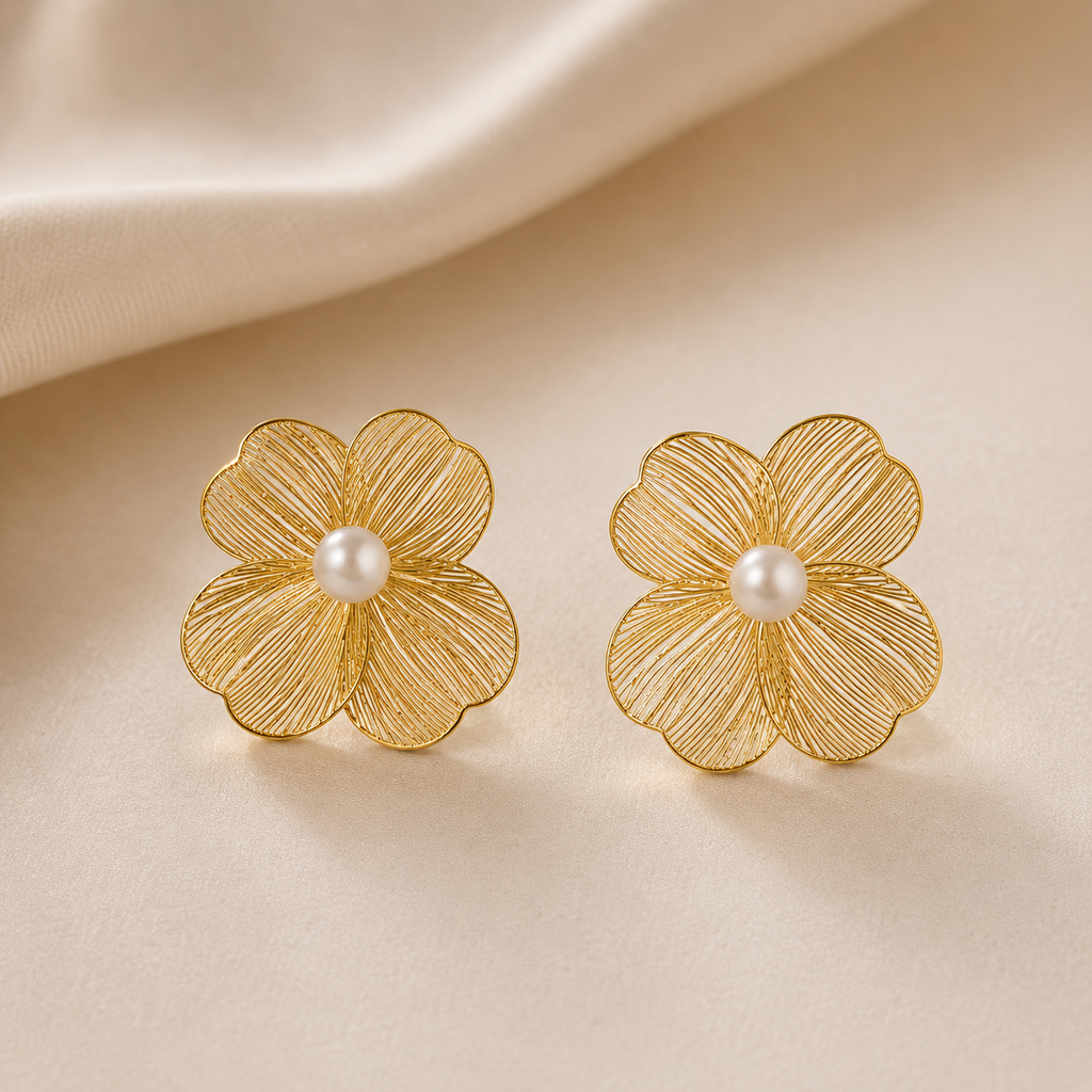Golden flower-shaped earrings with pearl centers on a beige fabric background