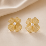 Golden flower-shaped earrings with pearl centers on a beige fabric background