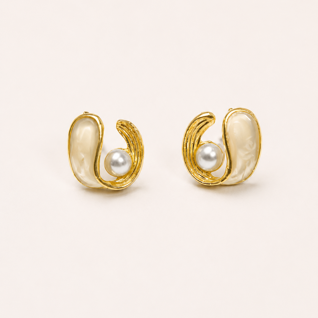Gold tone earrings with pearl centers on a beige background