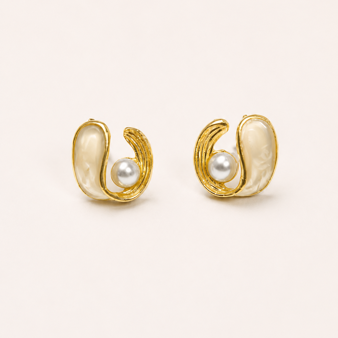 Gold tone earrings with pearl centers on a beige background