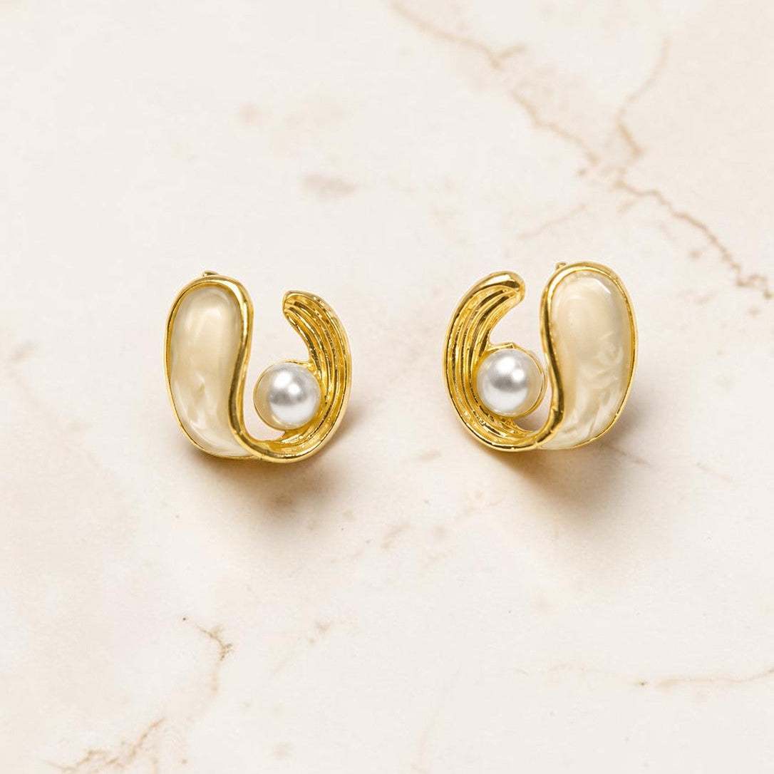Gold earrings with pearl centers on a beige marble background