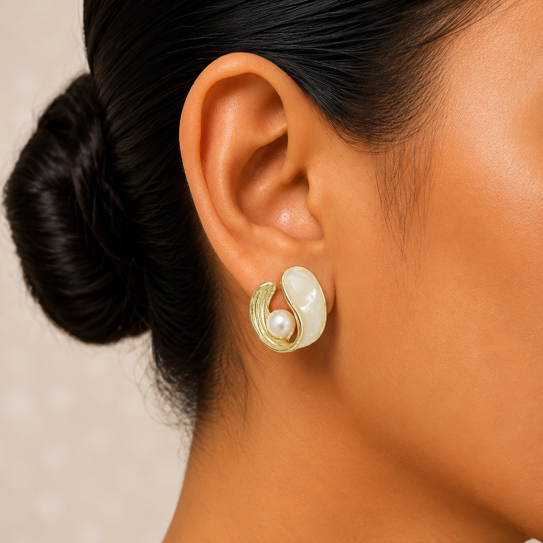 Close-up of an ear wearing a gold and pearl earring with a neutral background