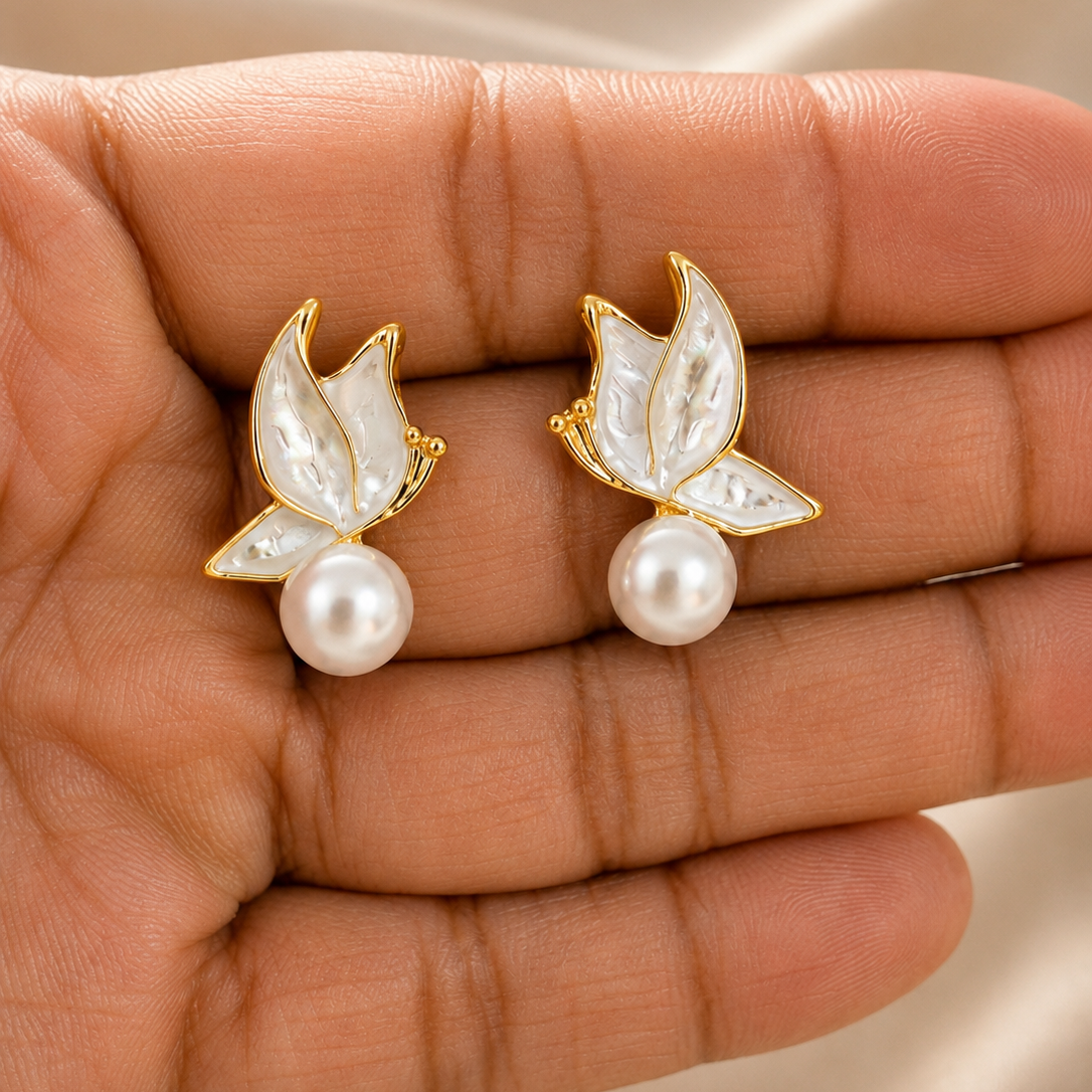 Gold tone and pearl earrings held in a hand against a beige fabric background