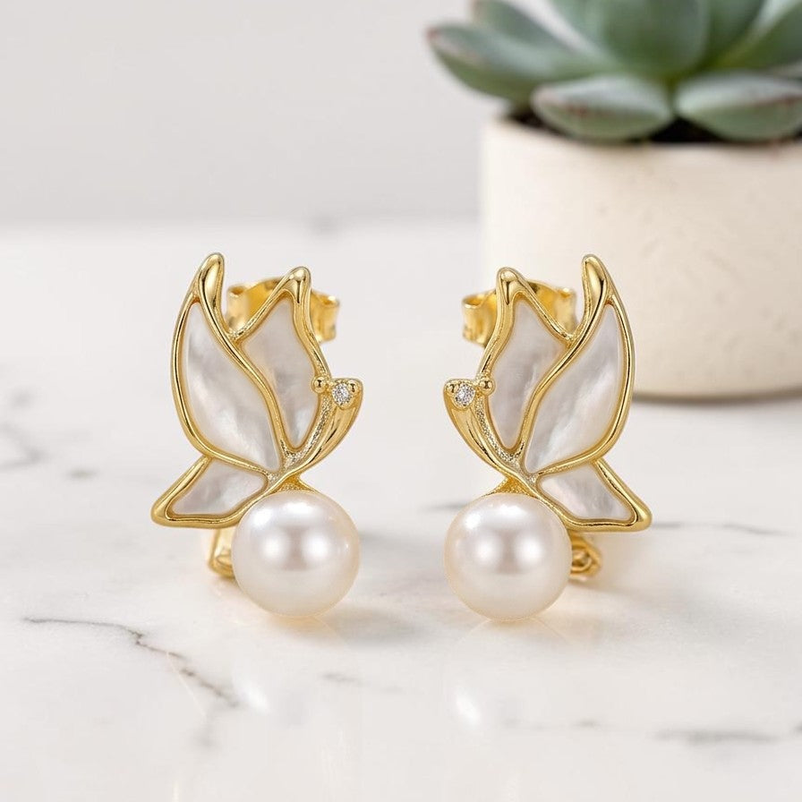 Gold-framed pearl earrings on a marble surface with a succulent plant in the background.