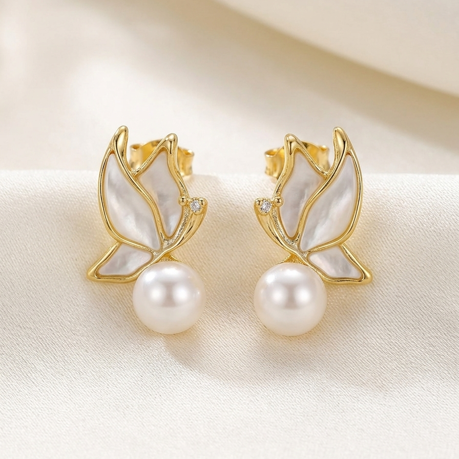 Gold tone earrings with pearl beads on a beige fabric background