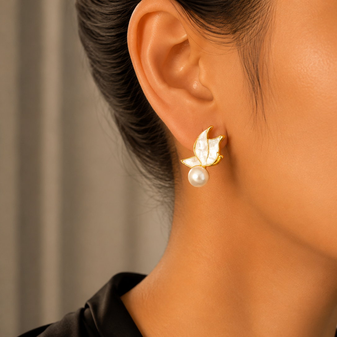 Close-up of an ear wearing a gold earring with a pearl, against a neutral background.