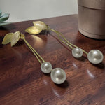 Gold tone and pearl hair accessories on a wooden surface with a plant in the background