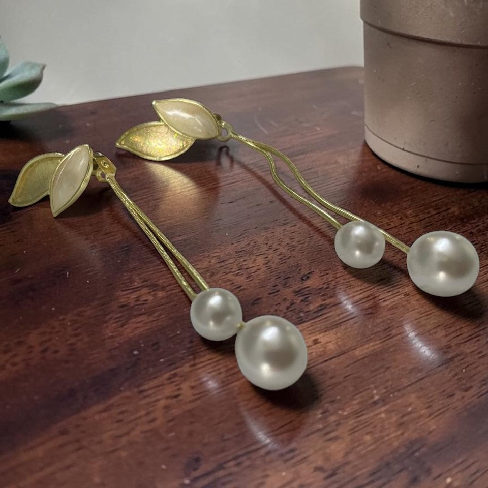Gold tone and pearl hair accessories on a wooden surface with a plant in the background