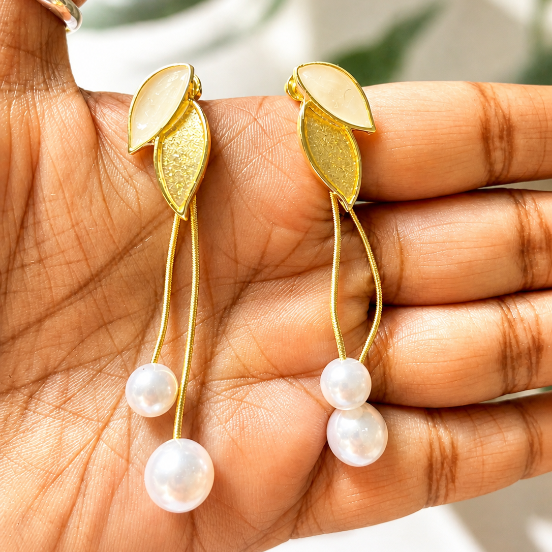 Golden leaf earrings with pearl drops held in a hand against a blurred natural background