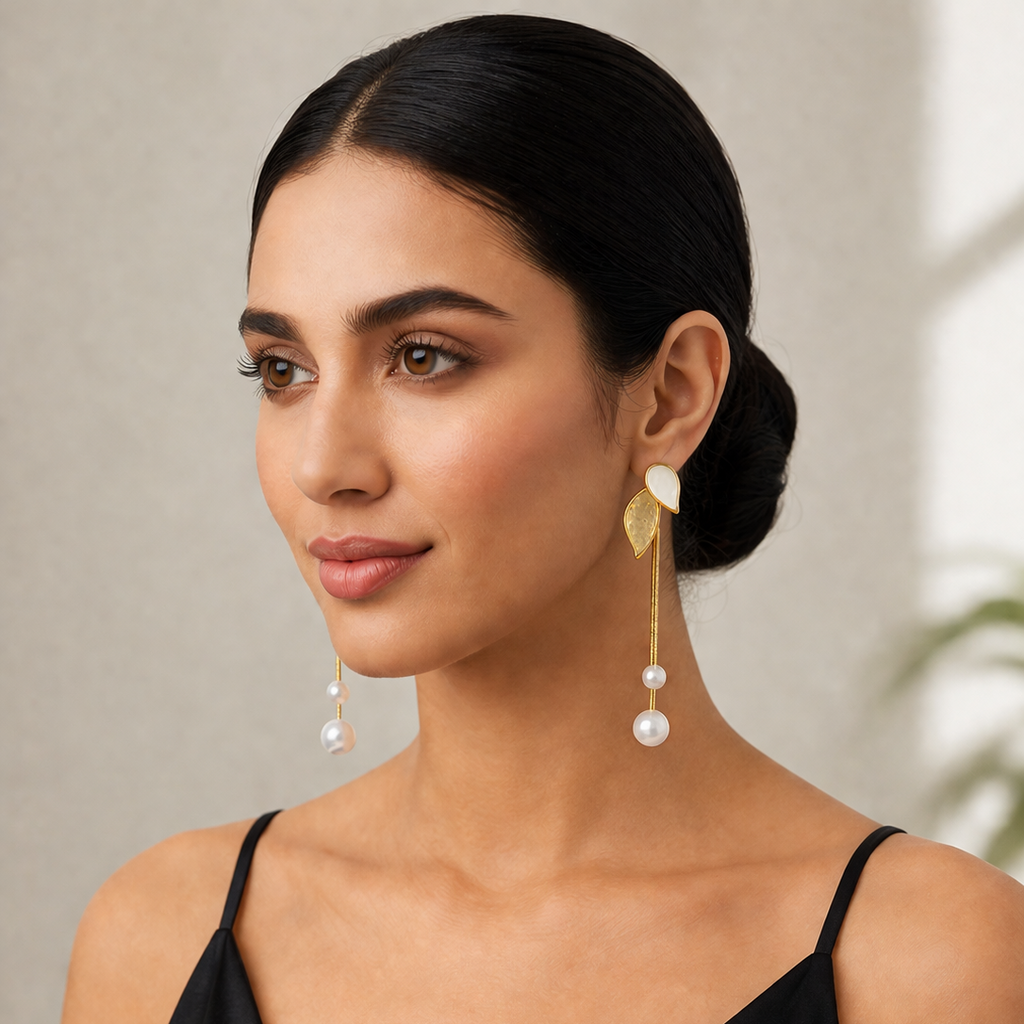 Woman wearing gold to ne earrings with pearl drops against a neutral background