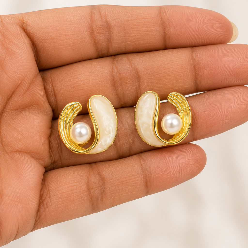 Gold tone and pearl earrings held in a hand against a neutral background