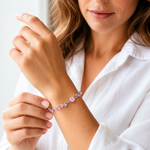 A close-up lifestyle shot of a woman wearing a delicate silver-toned bracelet adorned with small pink flowers and clear crystals, shown on her wrist.