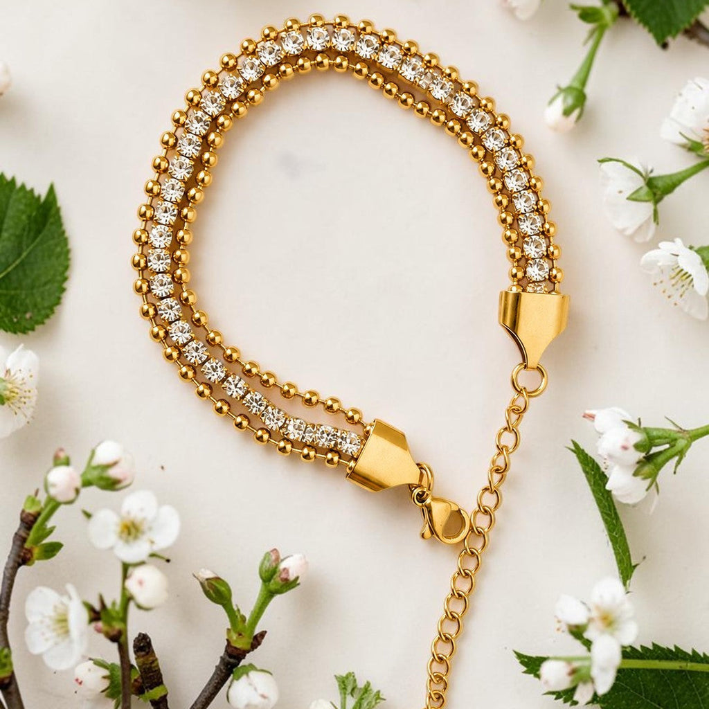 Gold tone bracelet with crystals on a white surface with flowers and leaves