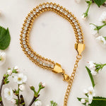 Gold tone bracelet with crystals on a white surface with flowers and leaves