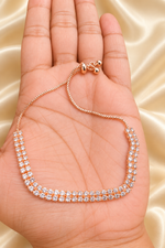 A rose gold double-row diamond tennis necklace displayed on a person's palm, set against a soft beige satin fabric background.