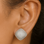 Silver textured earring worn on an ear with a blurred background