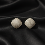 Pair of diamond-shaped silver earrings on black fabric