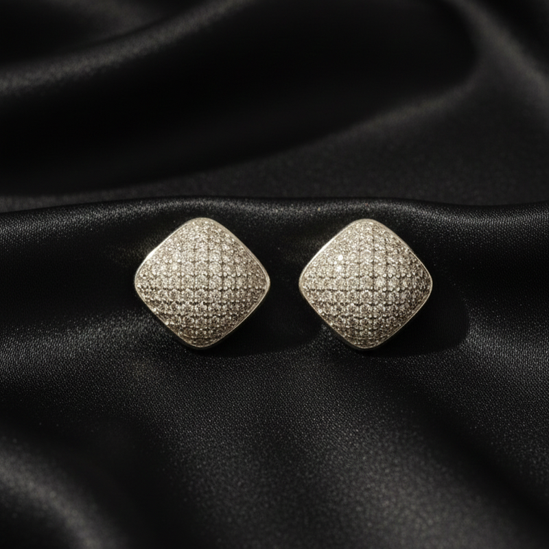 Pair of diamond-shaped silver earrings on black fabric