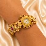 An ornate gold-toned wristwatch with a decorative bracelet, shown worn on a person's wrist against a draped champagne satin background.