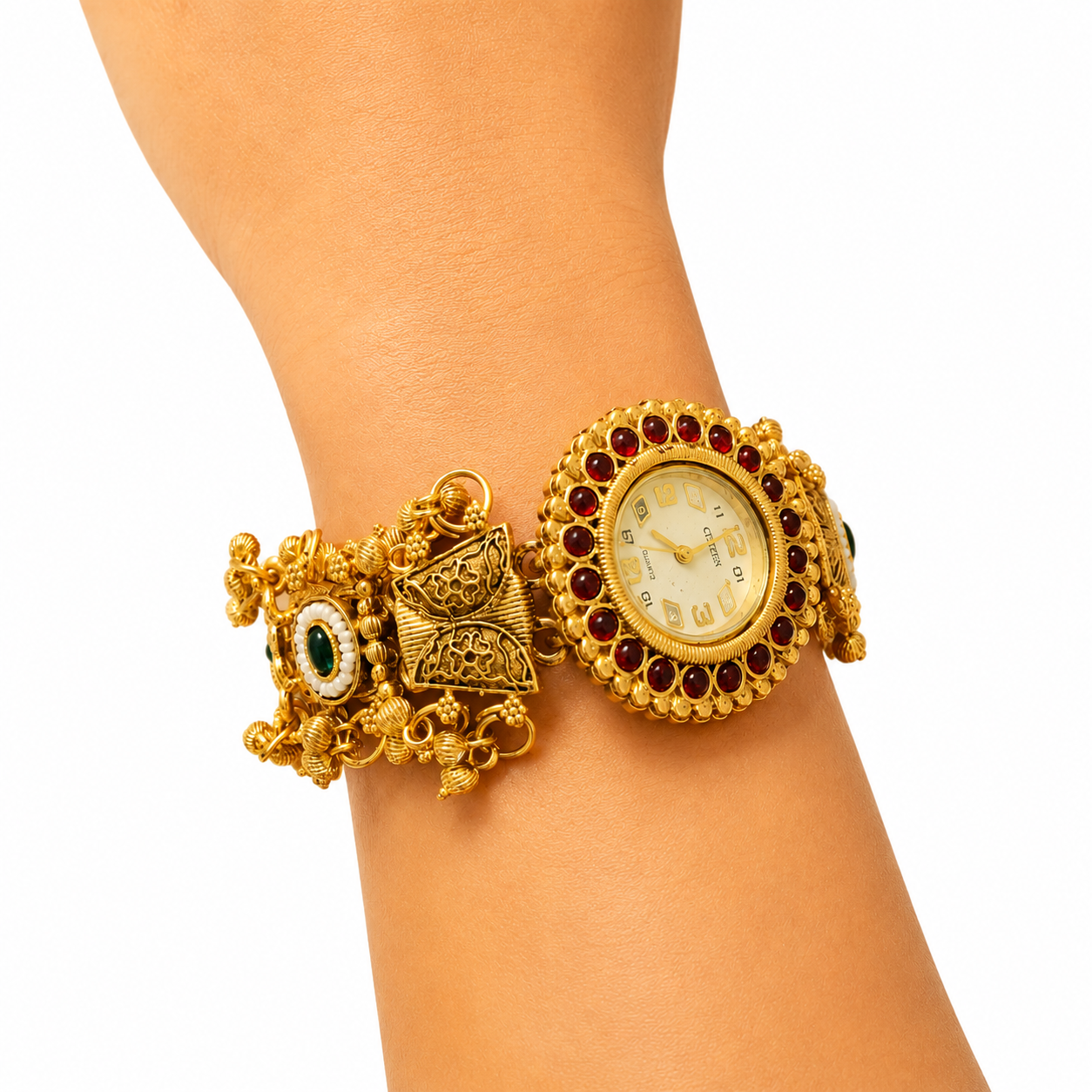 An ornate gold-toned cuff watch bracelet with a round dial, surrounded by dark red stones, and additional decorative elements including a bow charm and green stone accent, shown worn on a wrist against a white background.