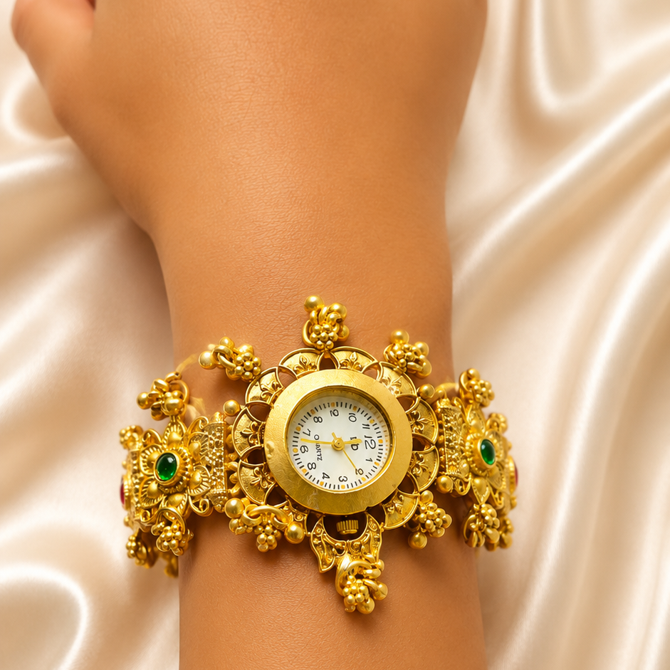 A close-up of a person's wrist wearing an ornate gold cuff watch with floral details and small green stone accents, set against a draped cream satin fabric background.