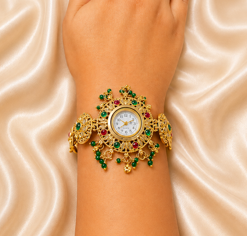 A close-up of a person's wrist and hand wearing an ornate gold watch with green and red gemstone embellishments, set against a draped beige satin fabric background.